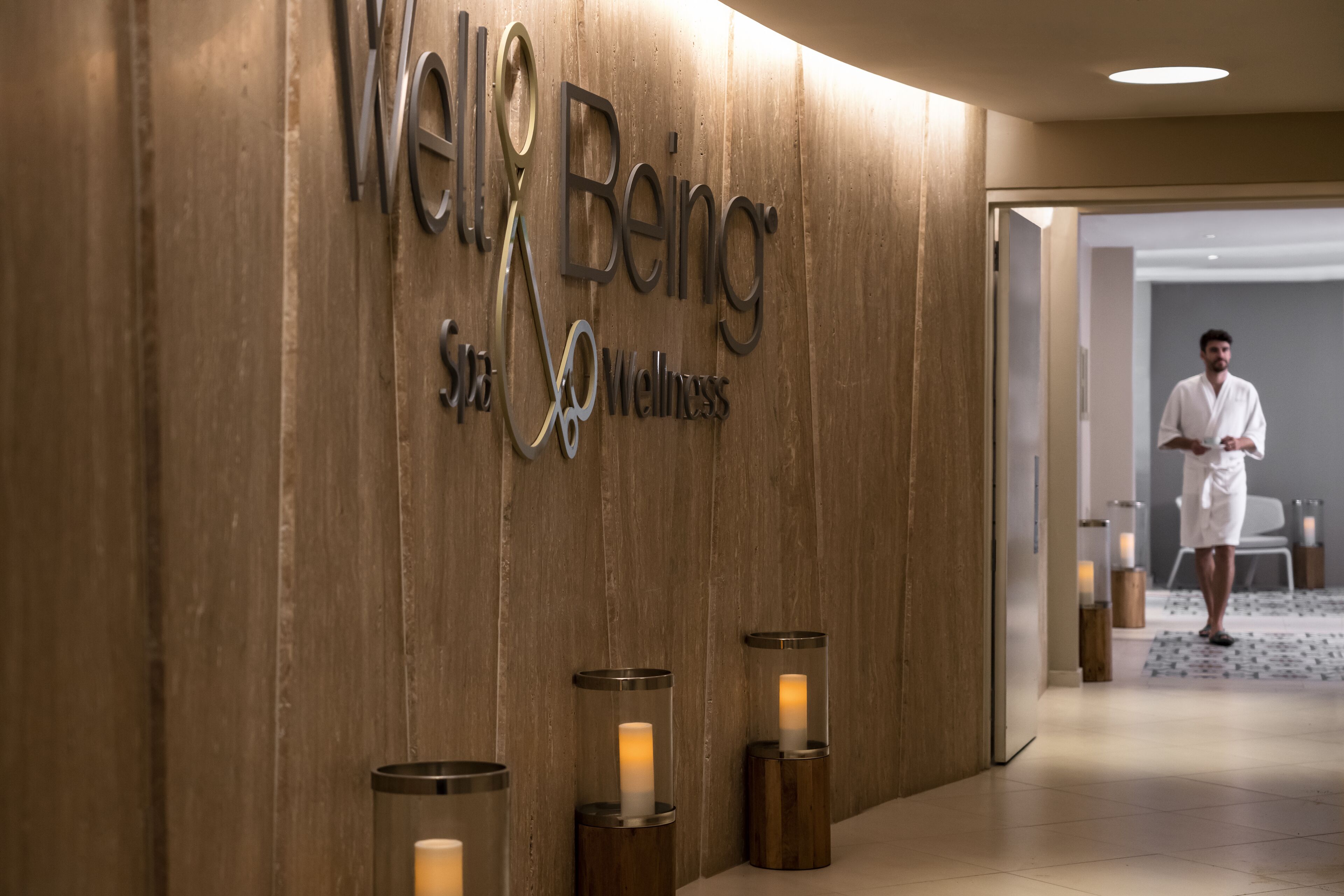 A wooden wall with the text "Well Being Spa Wellness" and three candle-like lights.