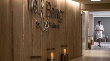 A wooden wall with the text "Well Being Spa Wellness" and three candle-like lights.
