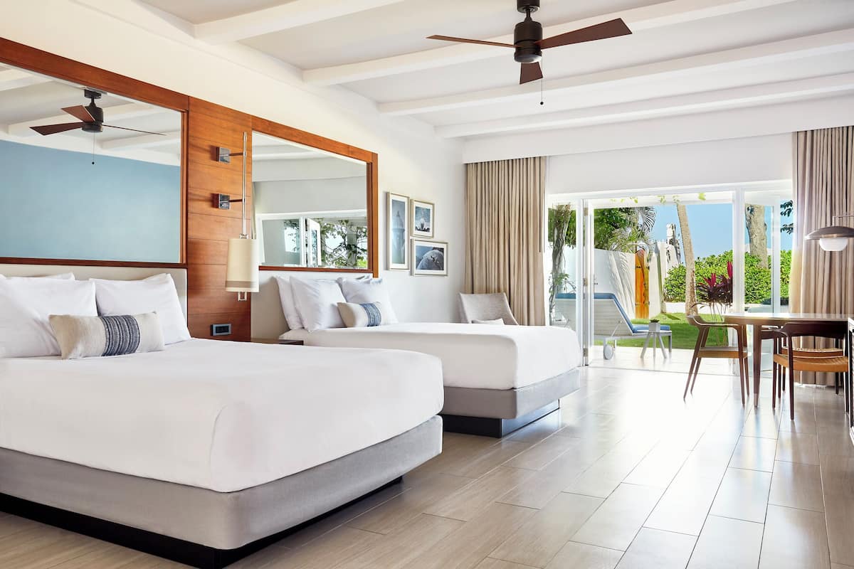 A modern hotel room with two beds, a dining area, and a balcony with a view.