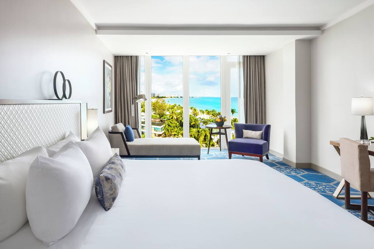 A hotel room with a large bed, a desk, a chair, and a view of the ocean.