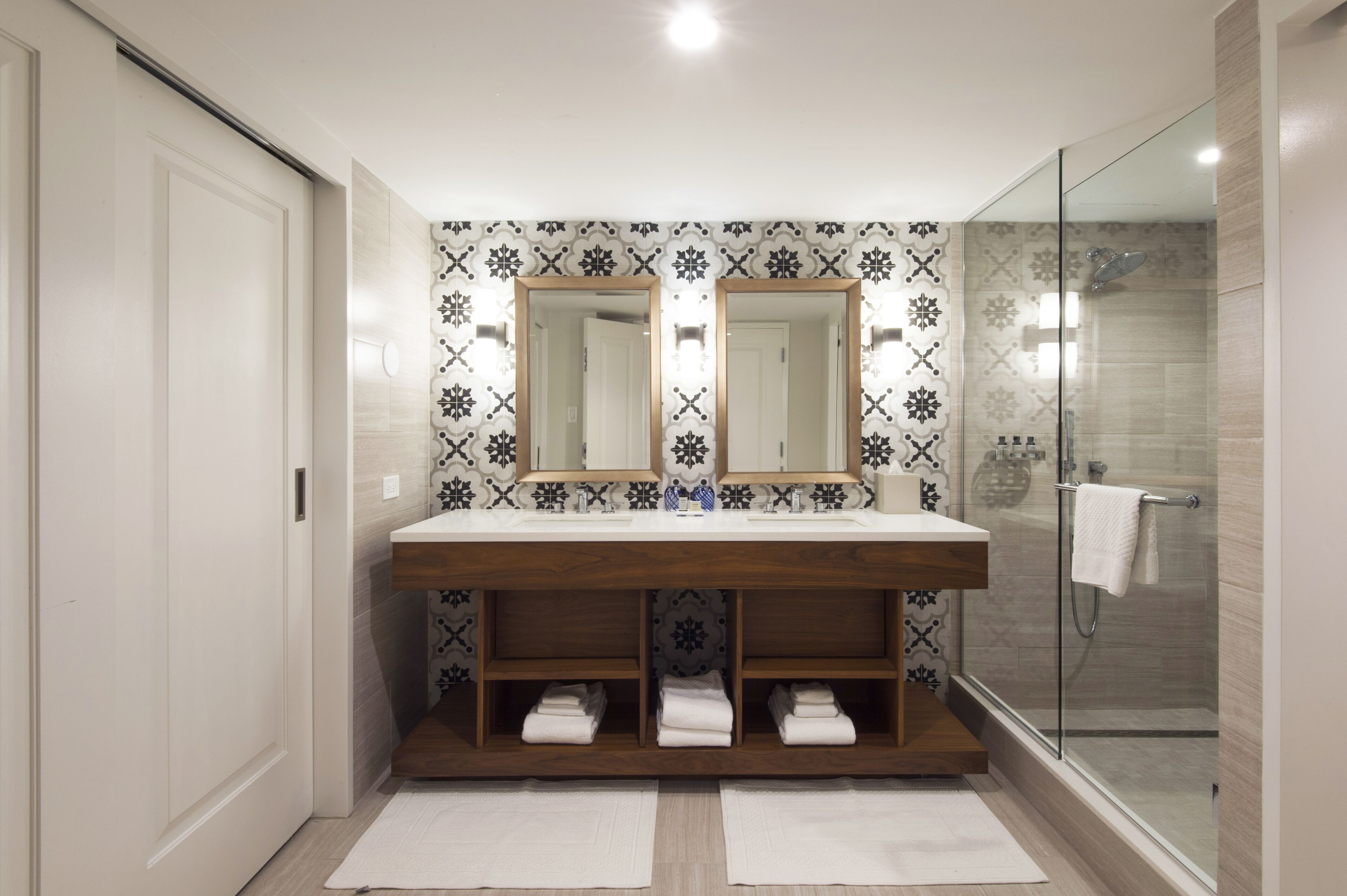 A modern bathroom with a double vanity, patterned backsplash, and a glass shower enclosure.