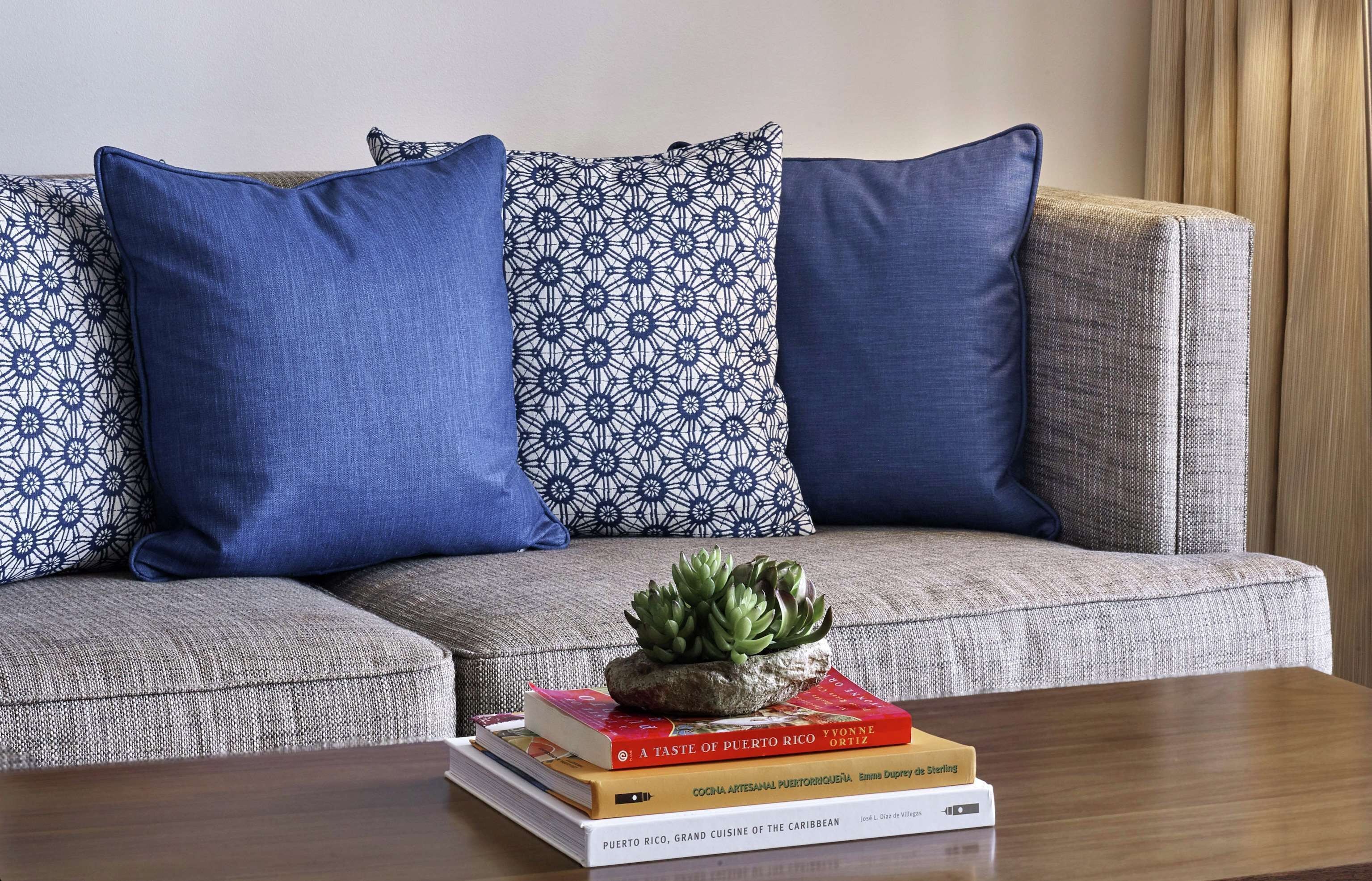 Un sofá modular con cojines estampados, una planta pequeña sobre una pila de libros y una mesa de centro de madera.