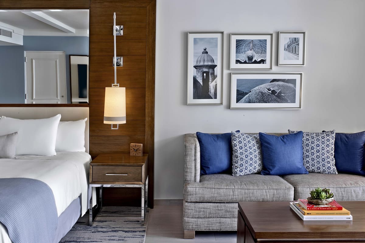 Une chambre d’hôtel moderne avec un lit, un mur d’accent en bois, une lampe fixée au mur, un canapé avec des coussins à motifs et des tableaux encadrés accrochés au mur.