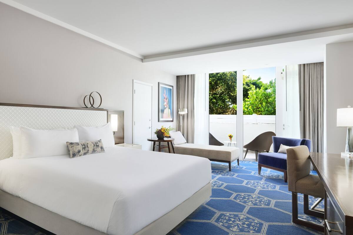 Une chambre d’hôtel avec un grand lit, un bureau, une chaise et une vue sur la verdure environnante.