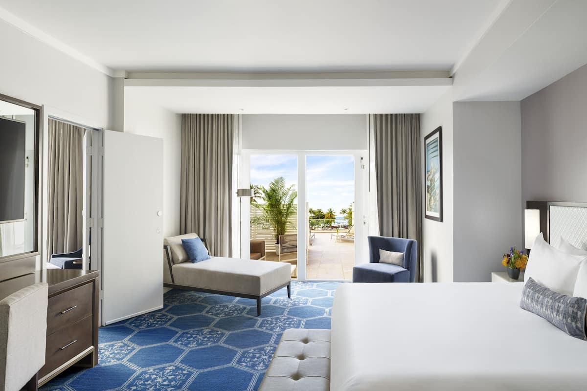 Une chambre d’hôtel avec un grand lit, un bureau, une chaise, une télévision et un balcon avec vue sur la plage.