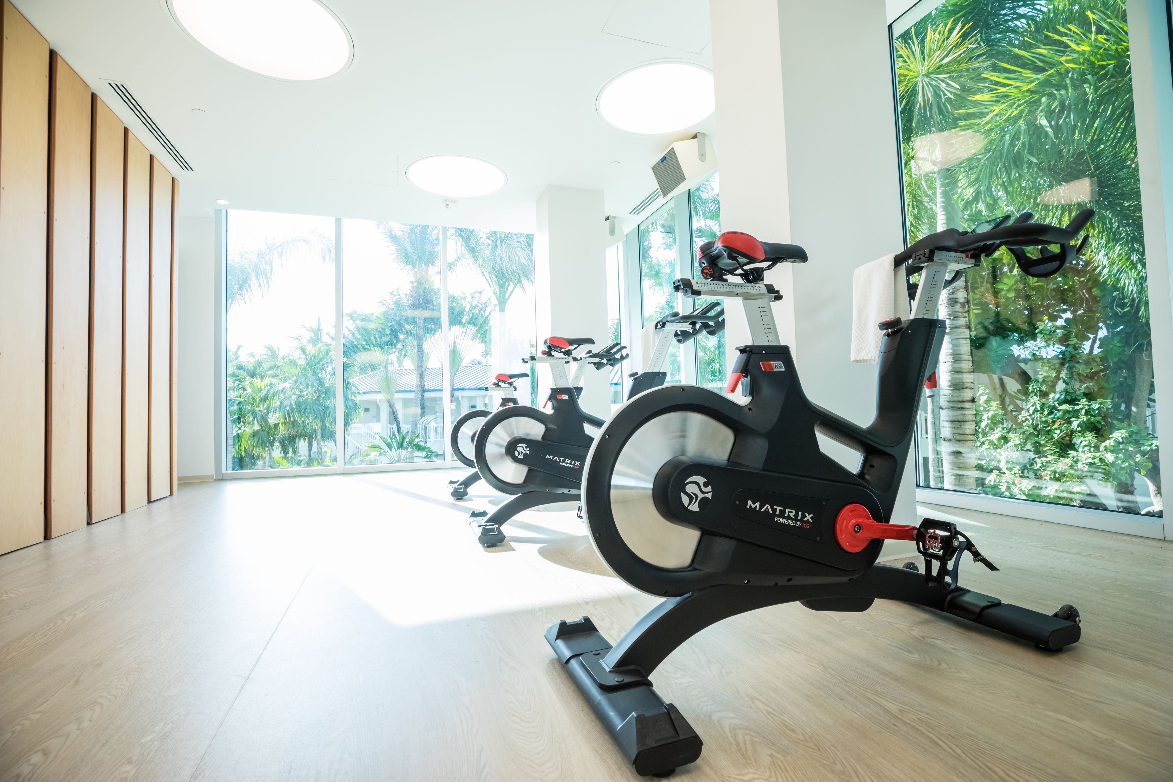Une salle de sport équipée de vélos d’appartement, dotée de grandes fenêtres et d’un plancher en bois.