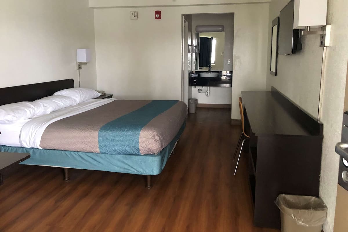 A hotel room with a bed, bedside table, lamp, and a view of the bathroom.