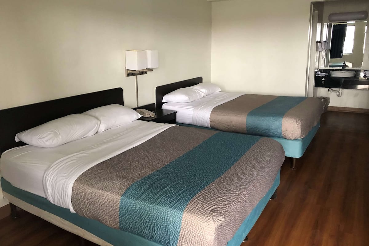 A hotel room with two beds, a nightstand with a lamp, a bathroom with a sink and mirror.