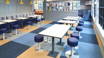 Una cafetería moderna con mesas altas y alfombra de estampado azul y naranja.
