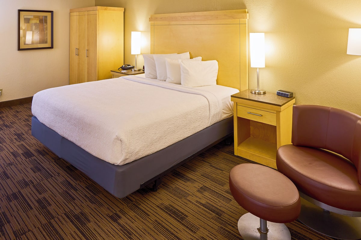 A hotel room with a bed, bedside tables, a chair, and a wardrobe.
