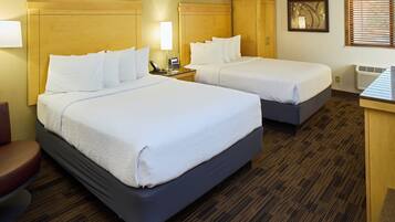 A hotel room with two beds, a desk, a chair, and a window with blinds.