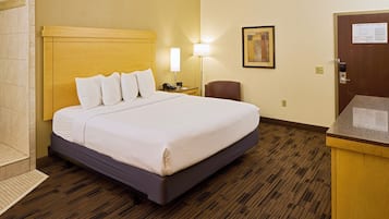 A hotel room with a bed, bedside lamp, chair, and a desk with a computer.