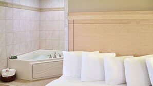 A hotel room with a large bed, a bathtub, and a small wicker basket with towels. - LivINN Hotel Minneapolis South / Burnsville (Burnsville)