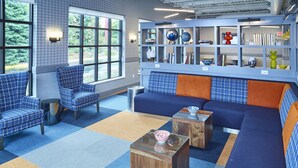 A modern lounge area with blue and orange patterned furniture, a glass coffee table, and a bookshelf with decorative items. - LivINN Hotel Minneapolis South / Burnsville (Burnsville)