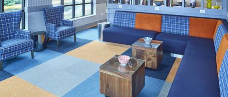 A modern lounge area with blue and orange patterned furniture, a glass coffee table, and a bookshelf with decorative items.