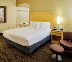 A hotel room with a large bed, a bedside table with a lamp, a chair, and a bathroom visible through an arched doorway.