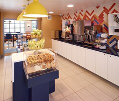 A breakfast bar with muffins and bananas, a coffee machine, and a patterned wall.