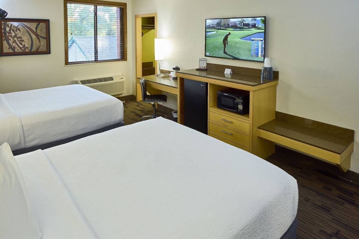 A hotel room with two beds, a desk with a television, a microwave, and a small refrigerator.