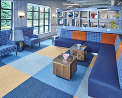 Una biblioteca con asientos azules y naranja, un ventanal grande y una estantería con diversos objetos.