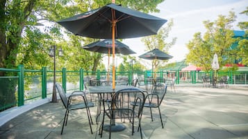 Un patio al aire libre con mesas y sillas, rodeado de cercas verdes y árboles.