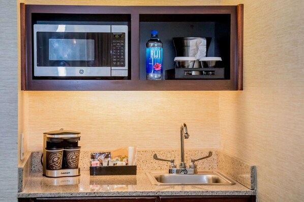 Una cocina compacta con microondas integrado, cafetera y una botella de agua.
