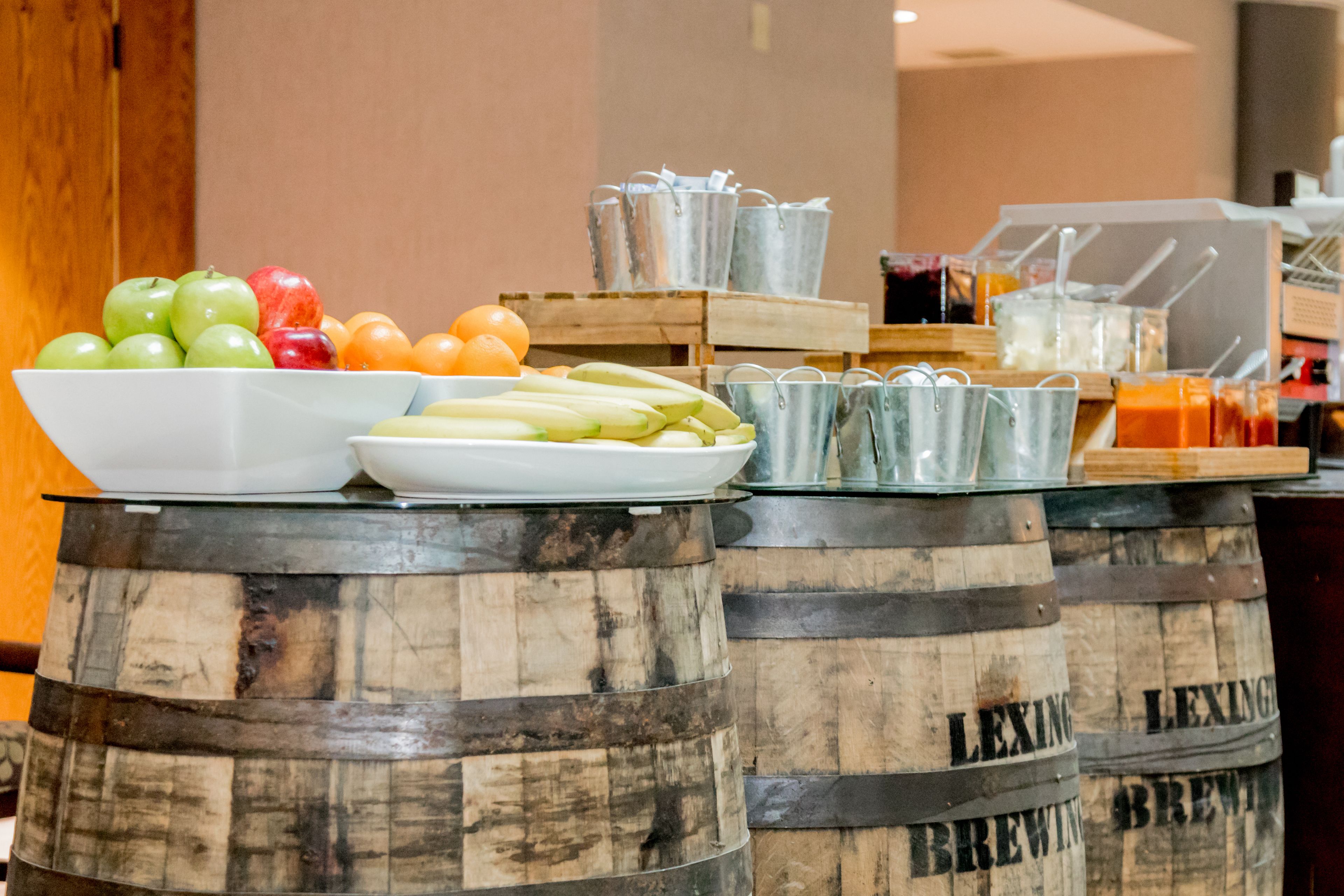 Um buffet de café da manhã com frutas, legumes e bebidas sobre barris de madeira identificados como 