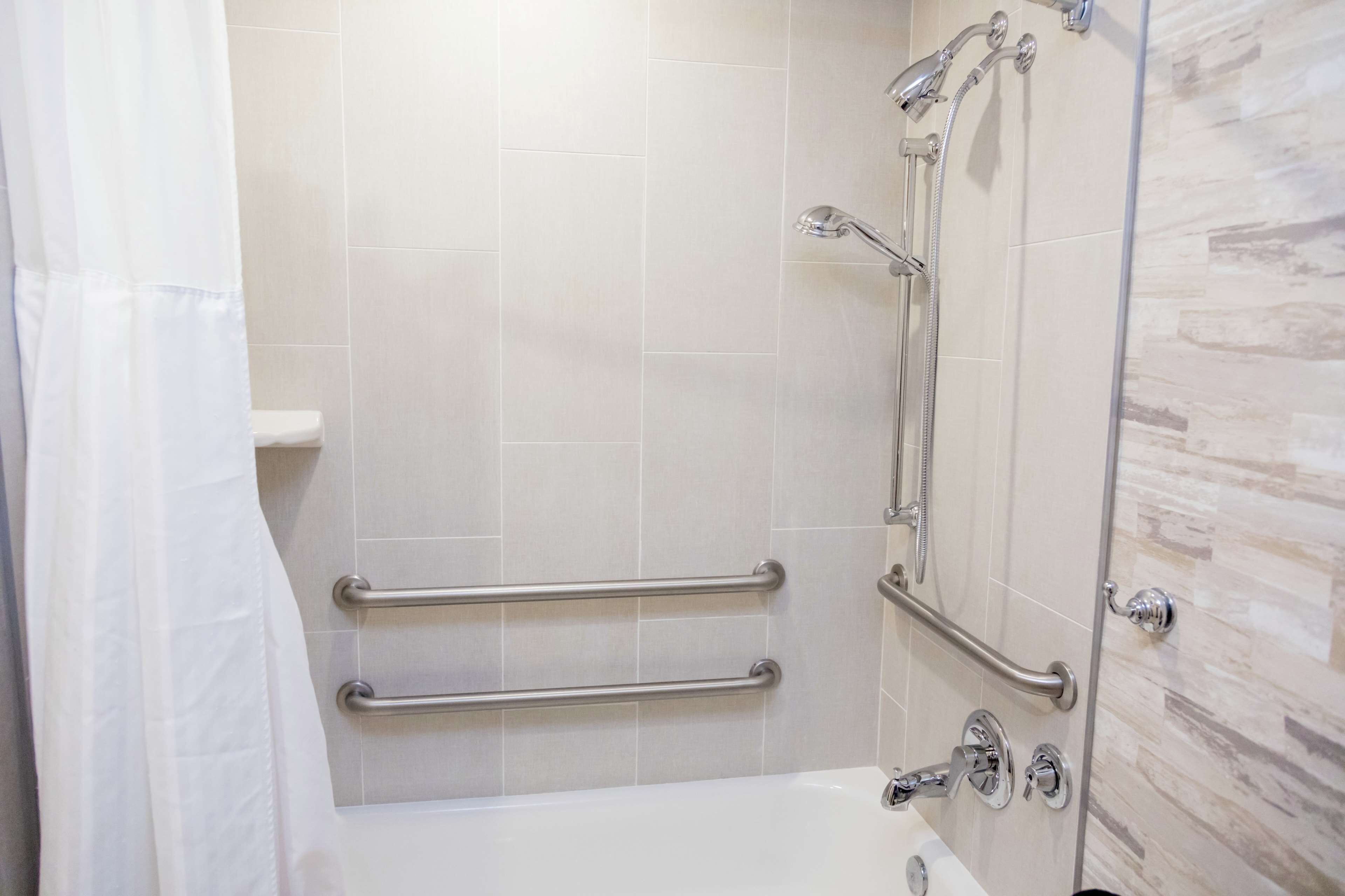 A bathroom with a bathtub, a shower with a glass door, and handrails.