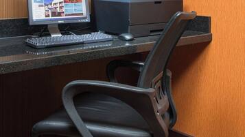 A desk with a computer, keyboard, and printer, a black office chair, and a telephone mounted on the wall.