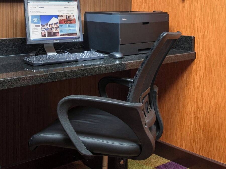 A desk with a computer, keyboard, and printer, a black office chair, and a telephone mounted on the wall.