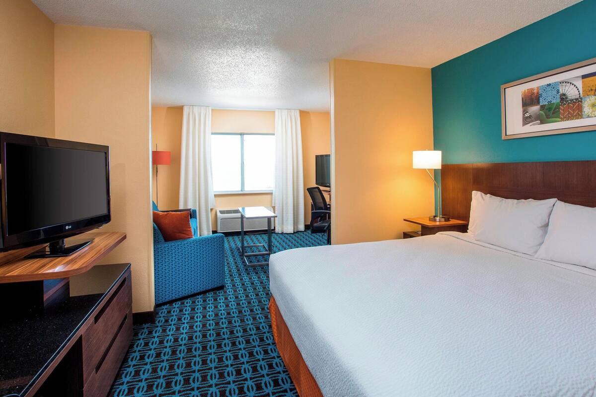 A hotel room with a large bed, a TV, a desk, and a chair.