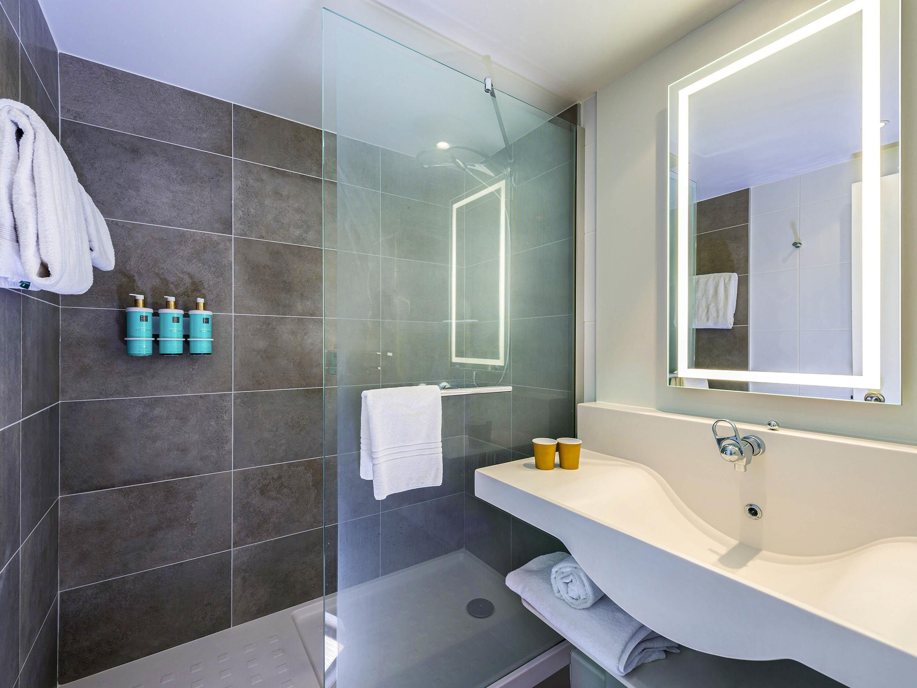 A modern bathroom with a glass shower enclosure, a large mirror, and a white sink.