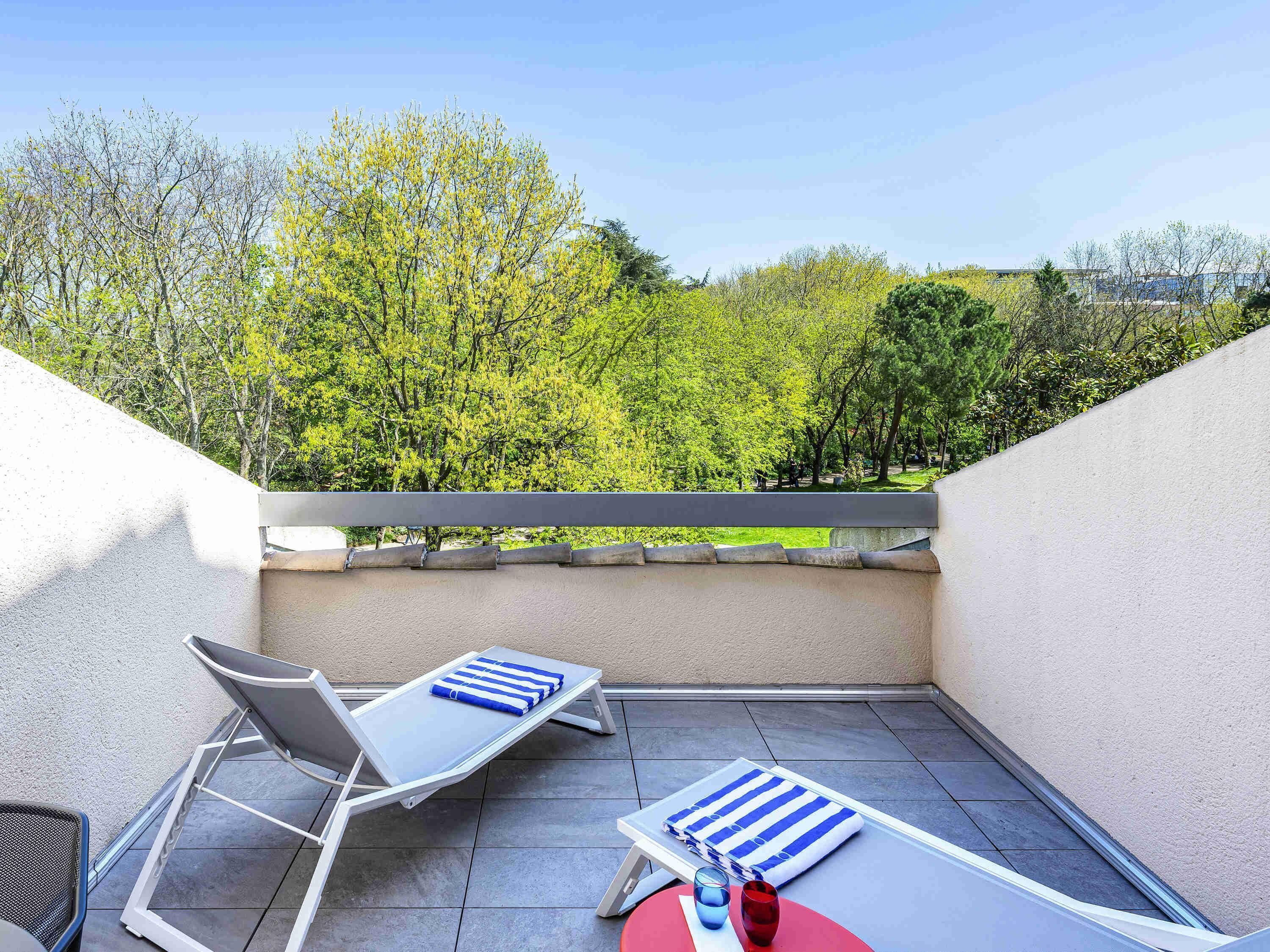Een balkon met een witte tafel, twee loungestoelen en een blauw gestreepte handdoek.