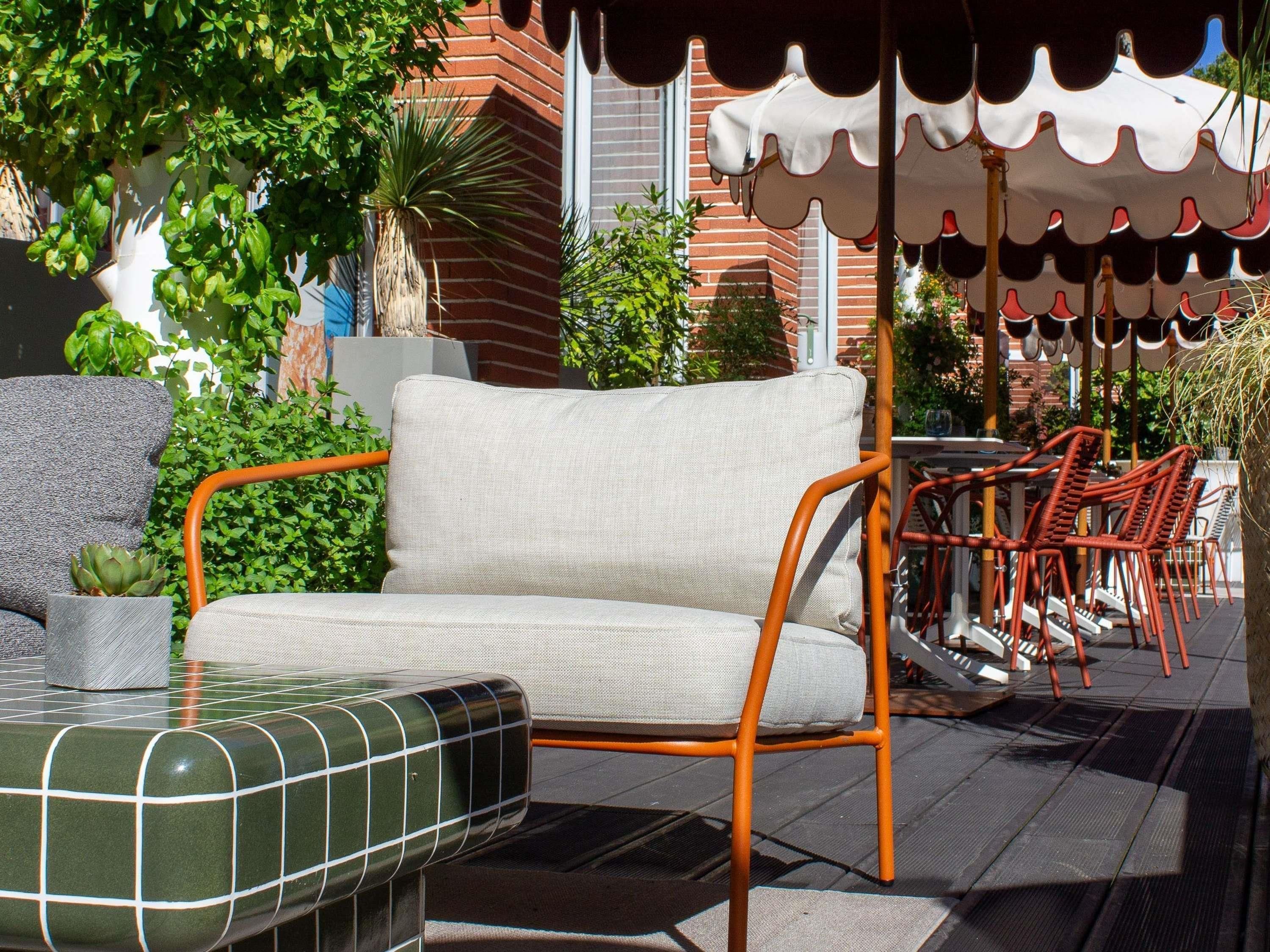 An outdoor seating area with a cushioned chair, a small table with a decorative tile top, and a patterned umbrella.