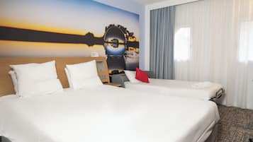 A hotel room with two beds, a nightstand, a red pillow, a painting of a sunset, and a window with curtains.