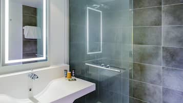 Un baño moderno con ducha envuelta en vidrio, tocador blanco con espejo y pared de azulejos.