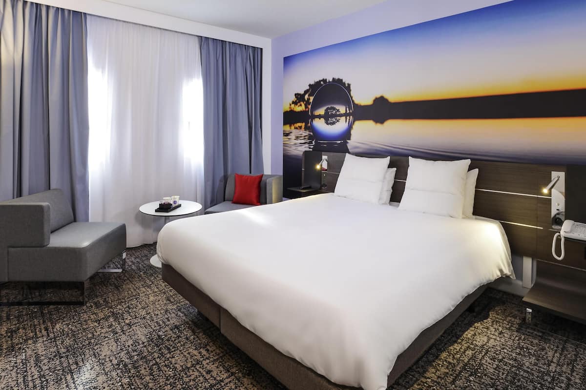 Une chambre d’hôtel avec un grand lit, un canapé, une petite table et un tableau représentant un coucher de soleil.