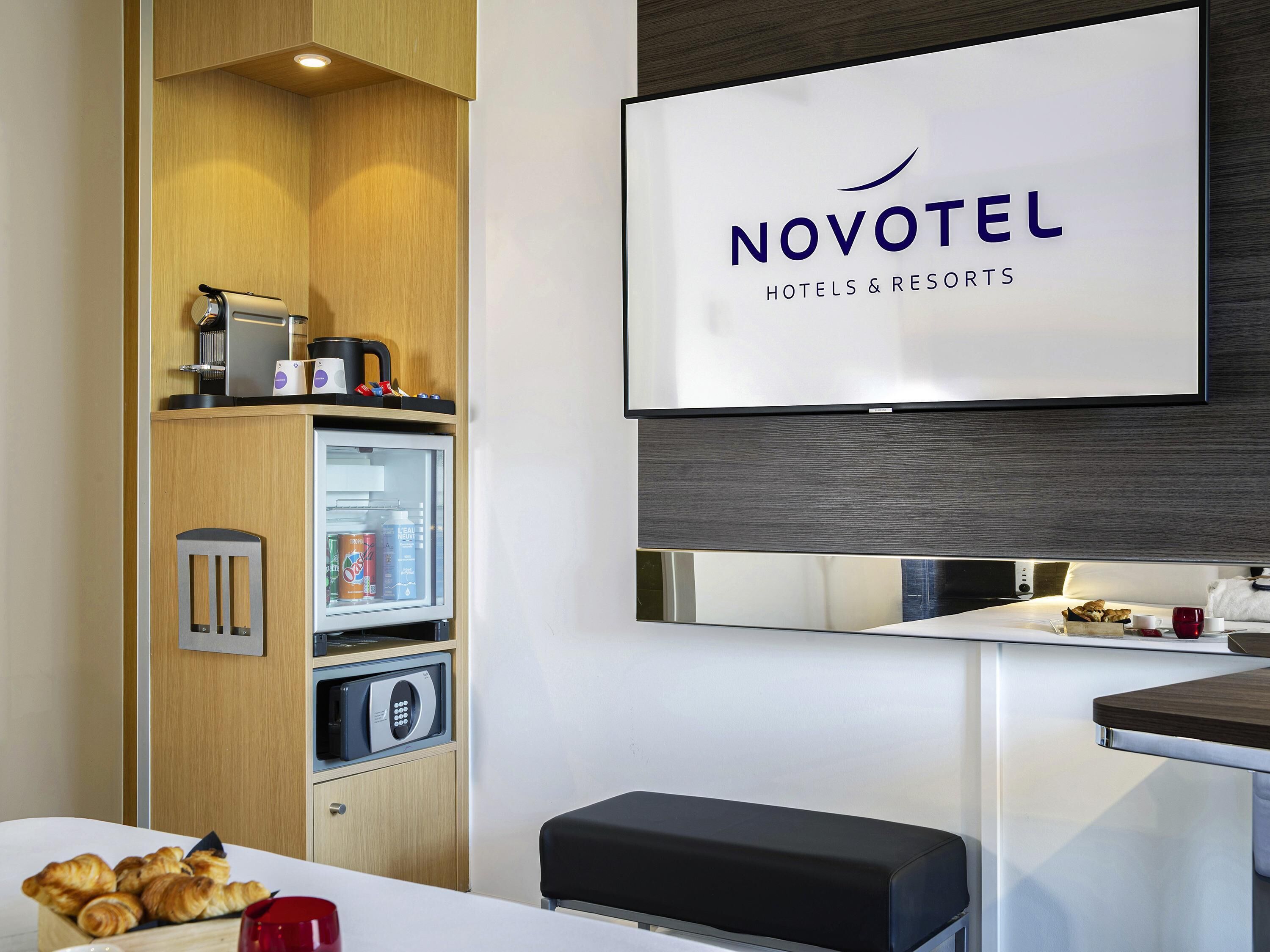 Une chambre d’hôtel Novotel équipée d’un minibar, d’une télévision, d’un four à micro-ondes et d’un coin petit-déjeuner.