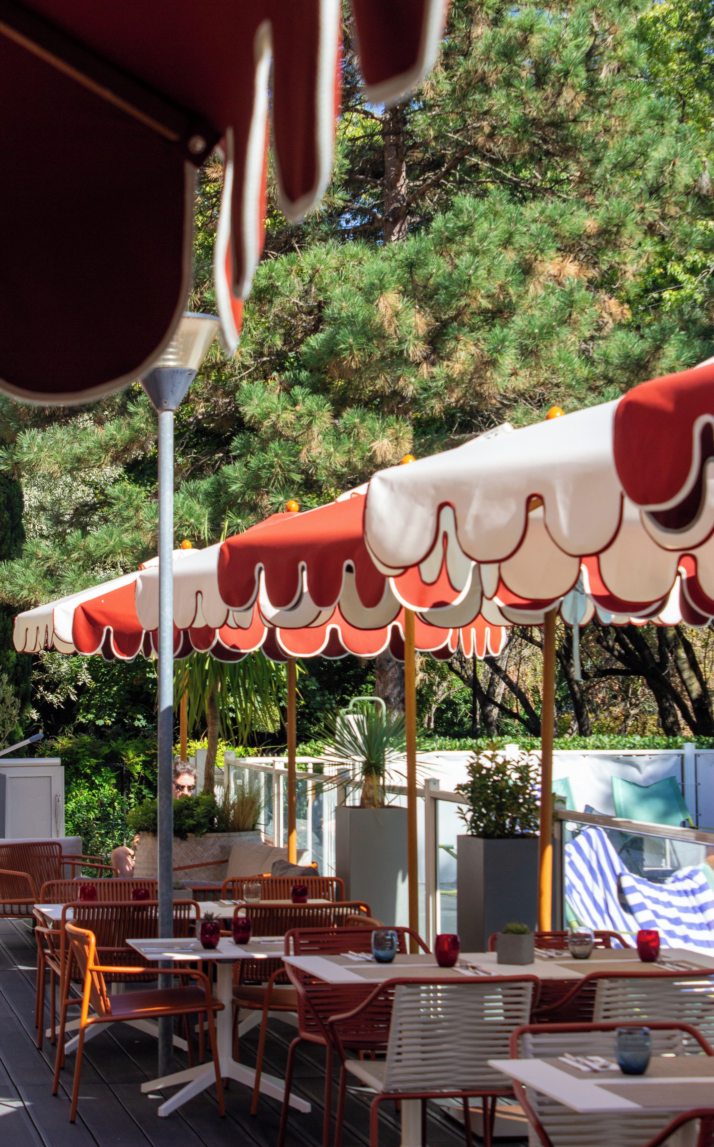 Outdoor seating with red and white umbrellas, surrounded by greenery.