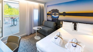 A hotel room with a bed, a sofa, a small table, and a view of a balcony with outdoor seating. - Novotel Toulouse Centre Compans Caffarelli (Toulouse)