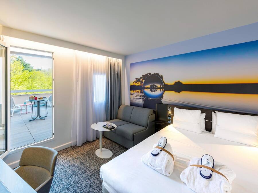 Camera d'albergo con un letto, un divano, un tavolino e vista su un balcone con posti a sedere.