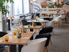 Un interior de restaurante moderno con varias mesas, sillas y plantas en macetas.