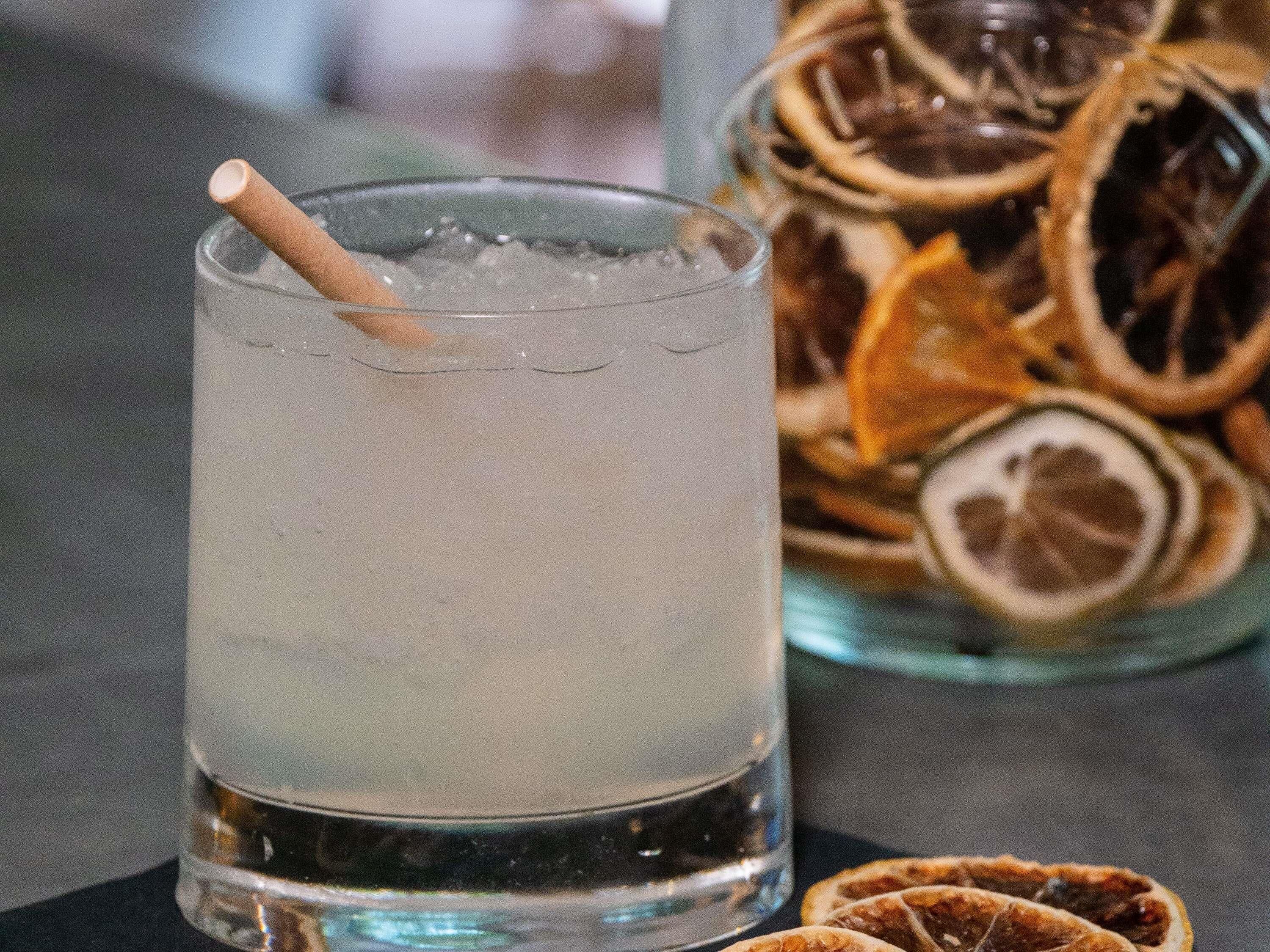 Un verre avec une paille, des glaçons et un arrière-plan flou avec des tranches d’orange séchées.