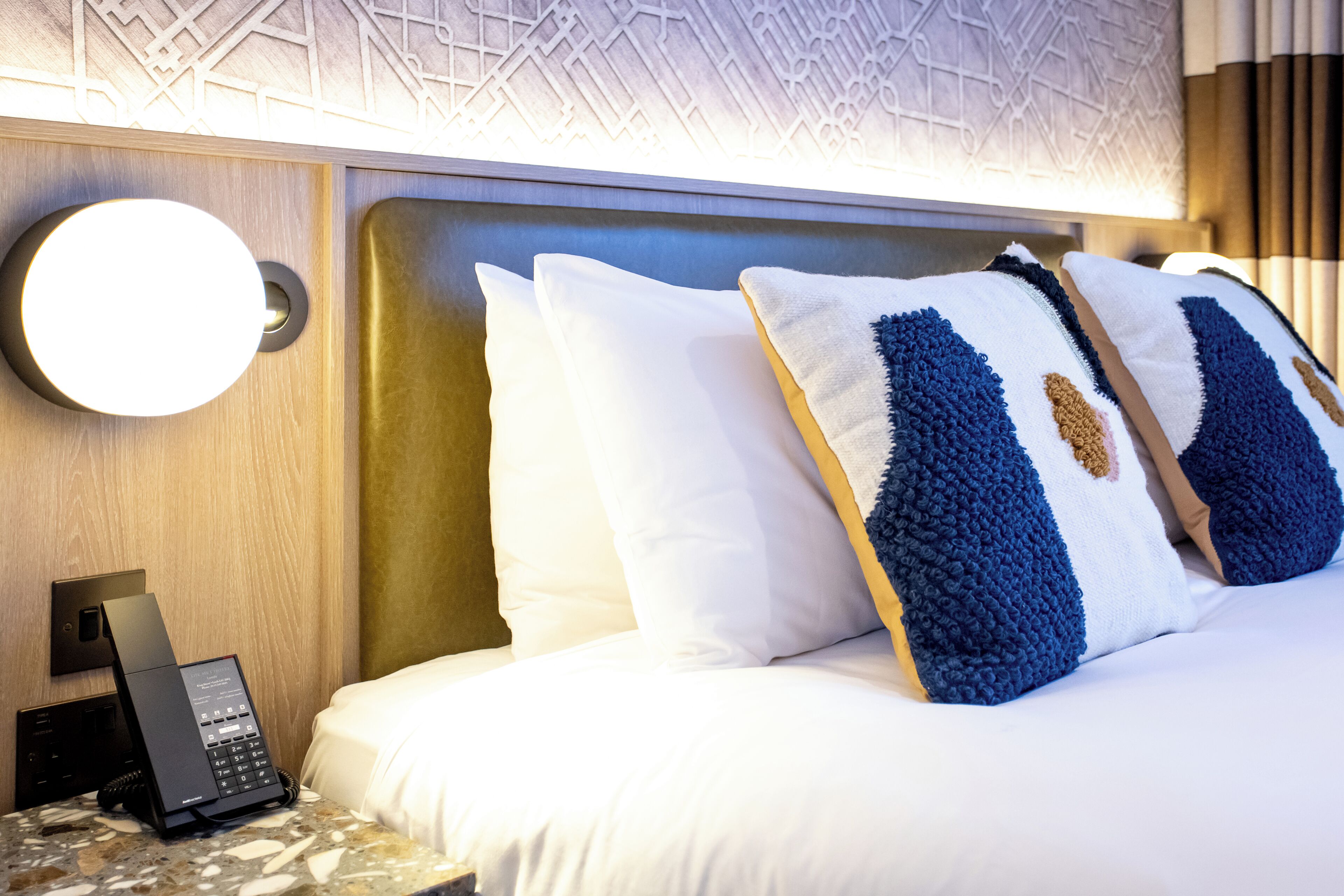 Una habitación de hotel con una cama, un teléfono en la mesita de noche y un aplique de pared.