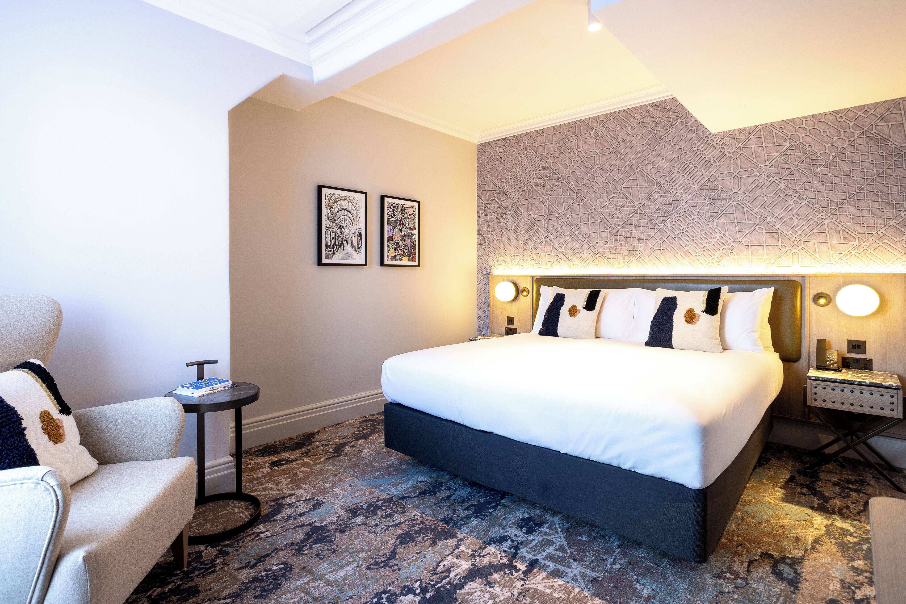 Una habitación de hotel moderna con una cama grande, una mesita auxiliar pequeña y una silla.