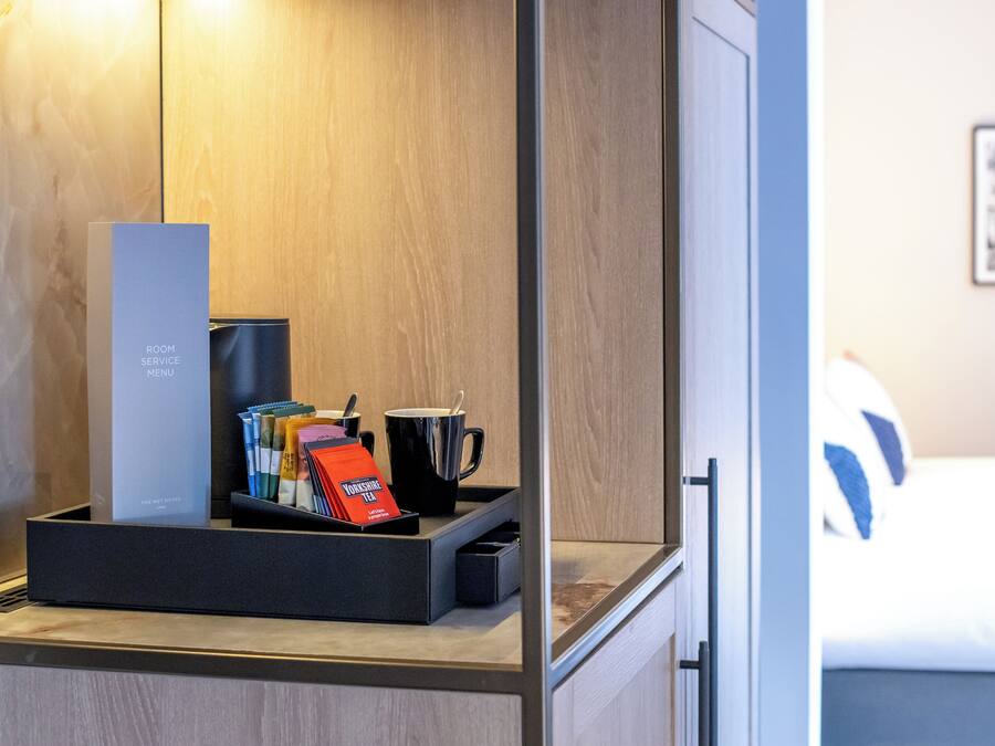 Ein Hotelzimmer mit einem Nachttisch, der eine schwarze Kaffeemaschine, eine schwarze Tasse, eine Packung Yorkshire Tea und ein Tablett mit verschiedenen Pflegeprodukten enthält.