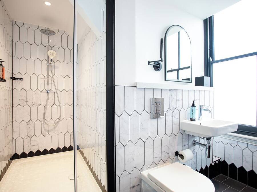 A modern bathroom with a shower, toilet, and sink, featuring hexagonal tile patterns and a large window.