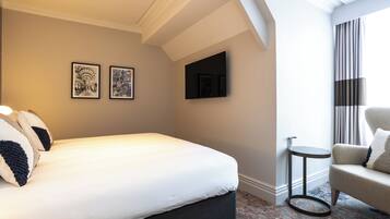 A hotel room with a bed, two framed artworks, a television, a small round table, and a chair.
