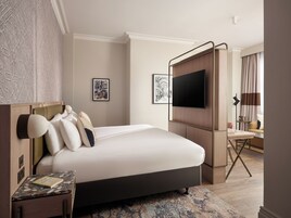 Una habitación de hotel moderna con una cama grande, un televisor de pantalla plana, un escritorio y una zona de estar con una lámpara.