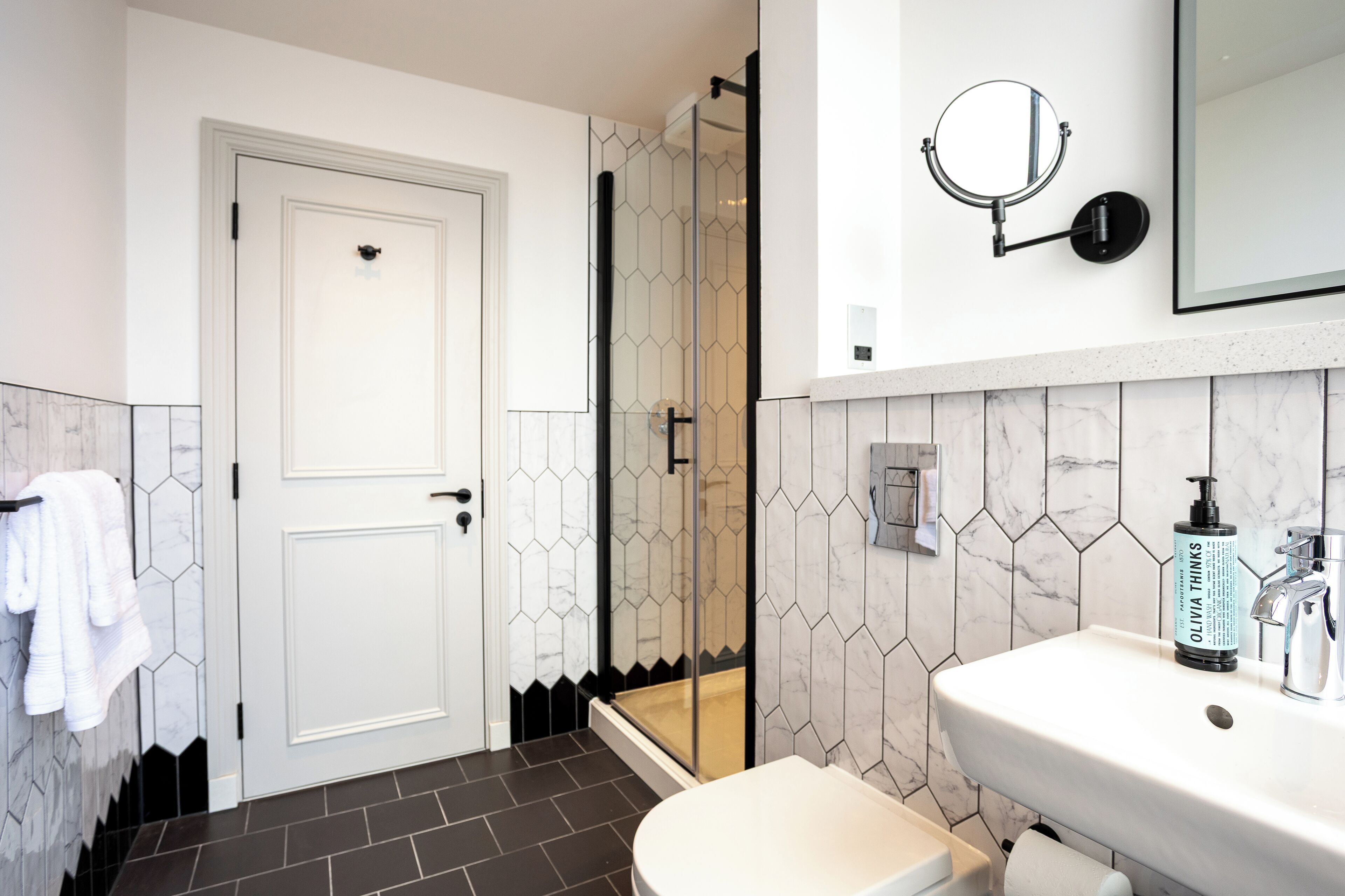 A bathroom with a white door, a shower, a sink, and a mirror.