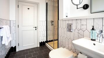 A bathroom with a white door, a shower, a sink, and a mirror.